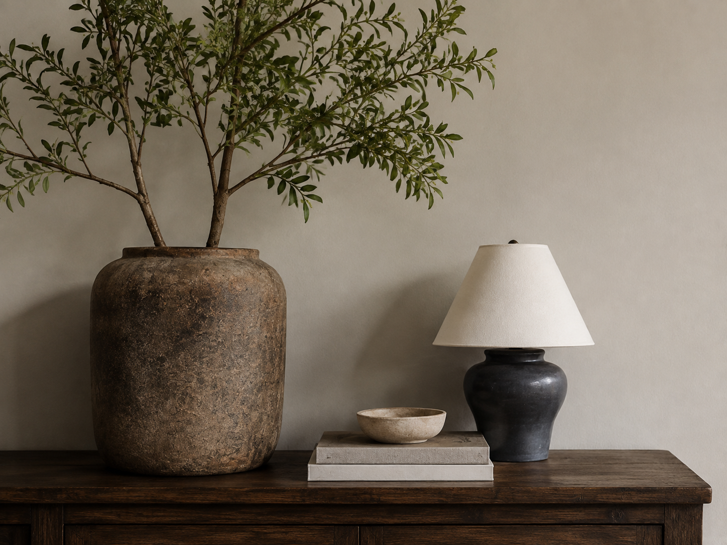 A dark wood console styled with a large ceramic vessel, books, and a table lamp